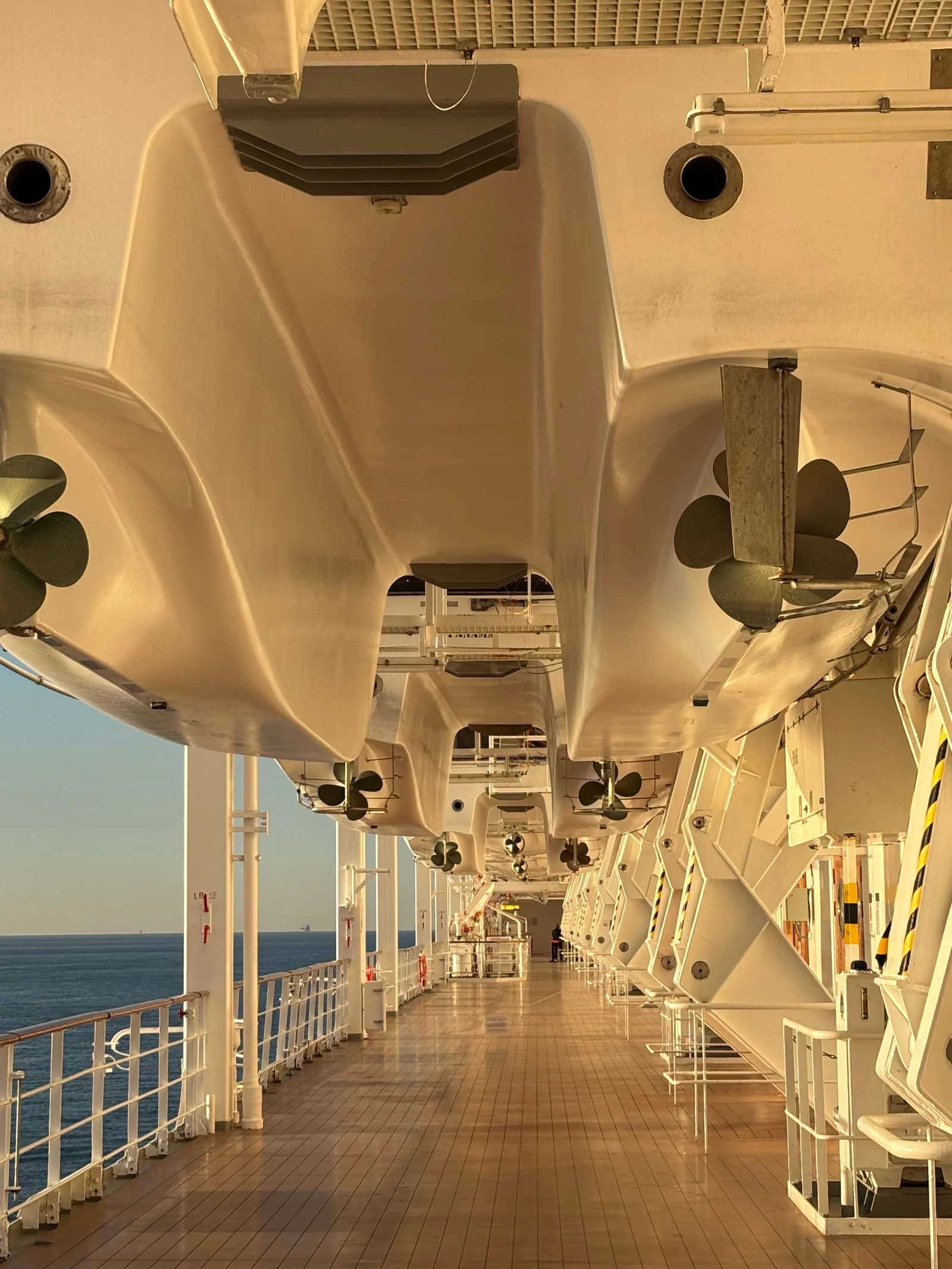 Empty cruise-ship promenade beneath lifeboats